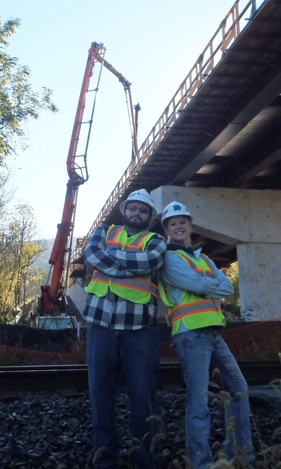Don Whipple and Maggie Jackson standing back to back in front of a bridge and crane.