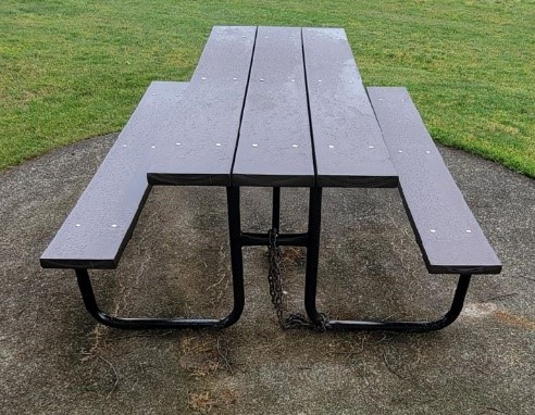 A gray plastic picnic table sits in a small dirt circle surrounded by grass
