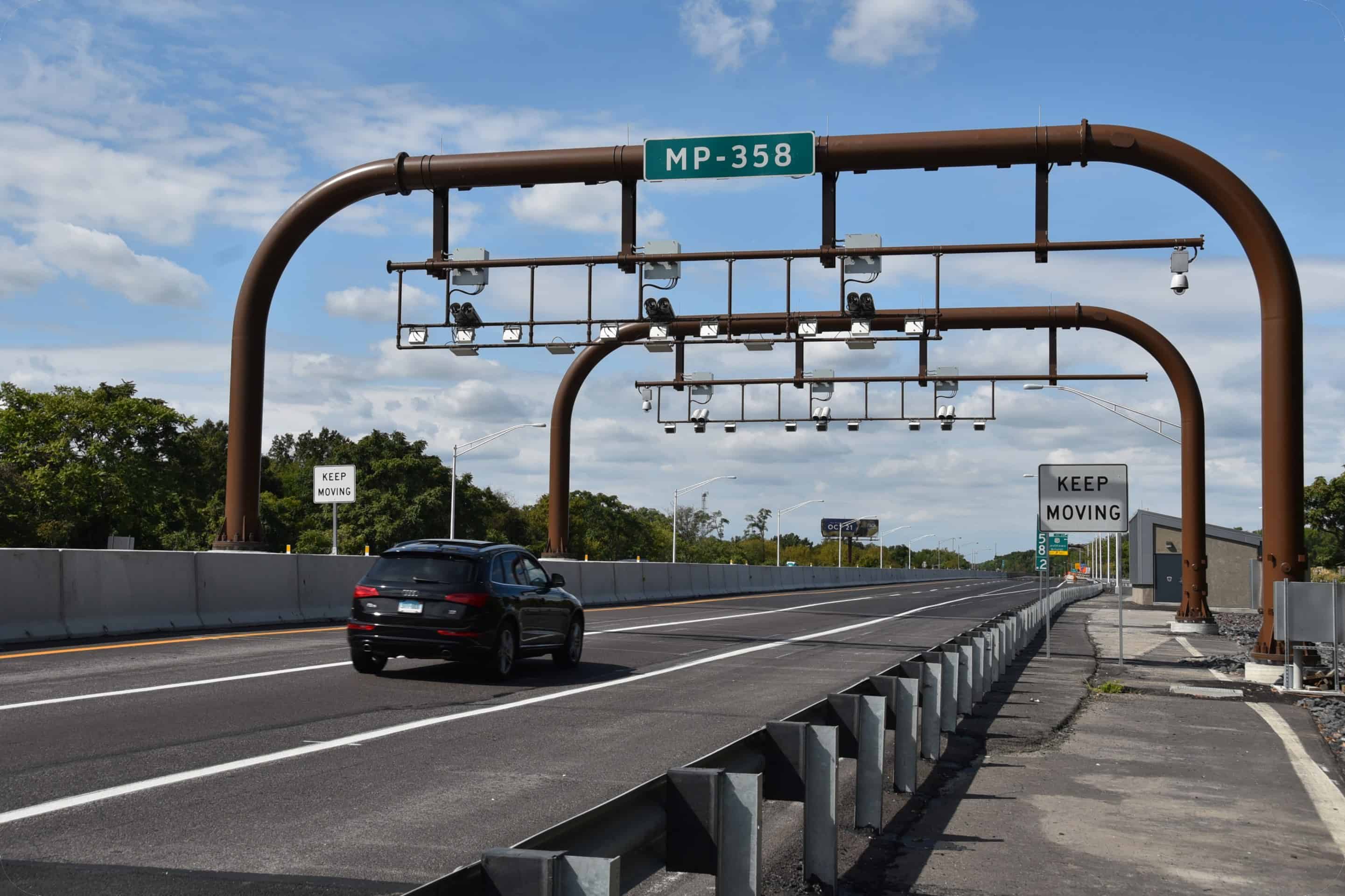 Two curved metal pipes with tolling camera devices extend over a highway.