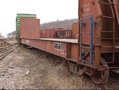 An image of an old rusty railroad flatbed car sitting along a train track.