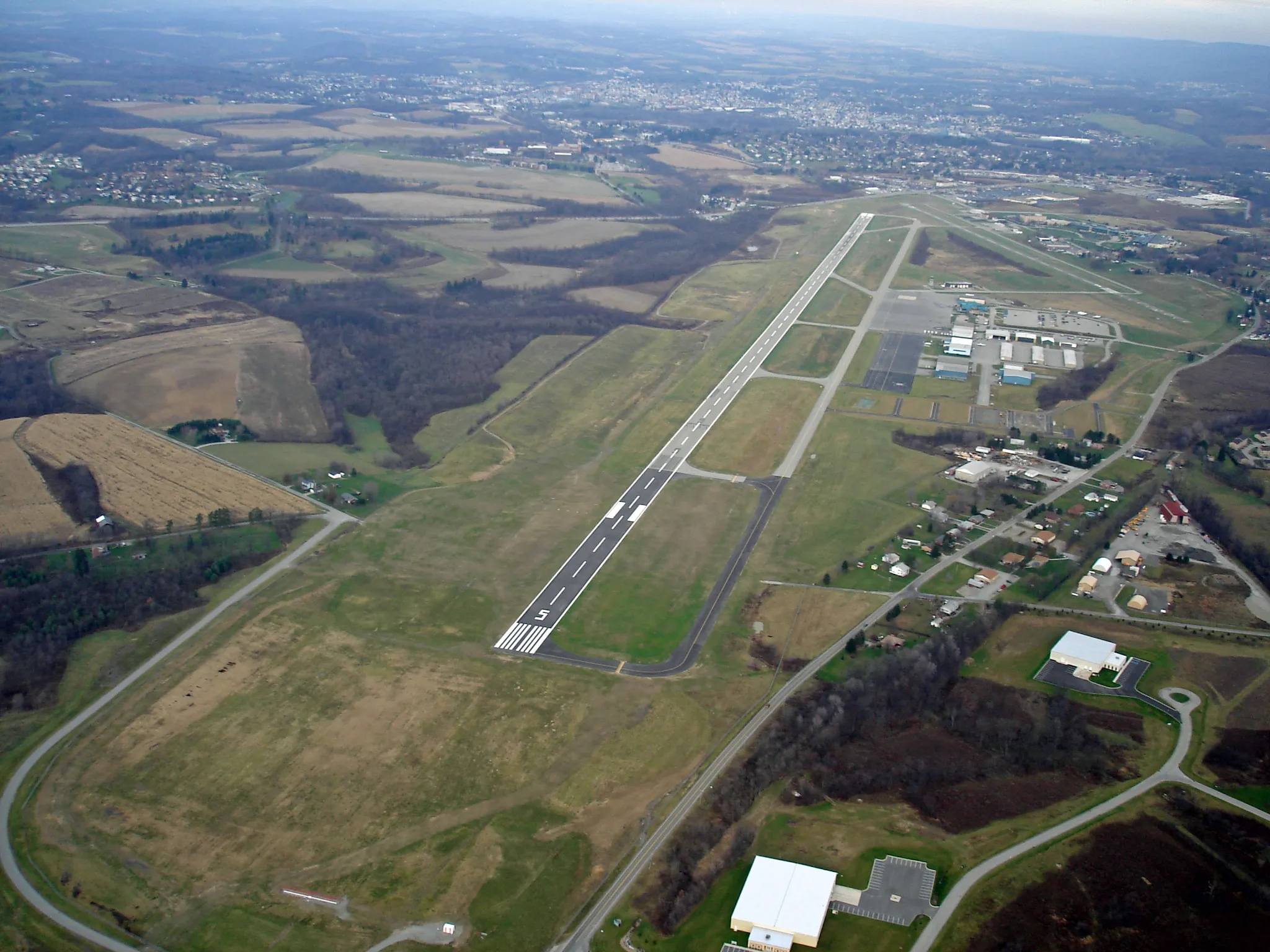 An aerial image of a rural airport and hangar with grassy fields and farmland on either side.