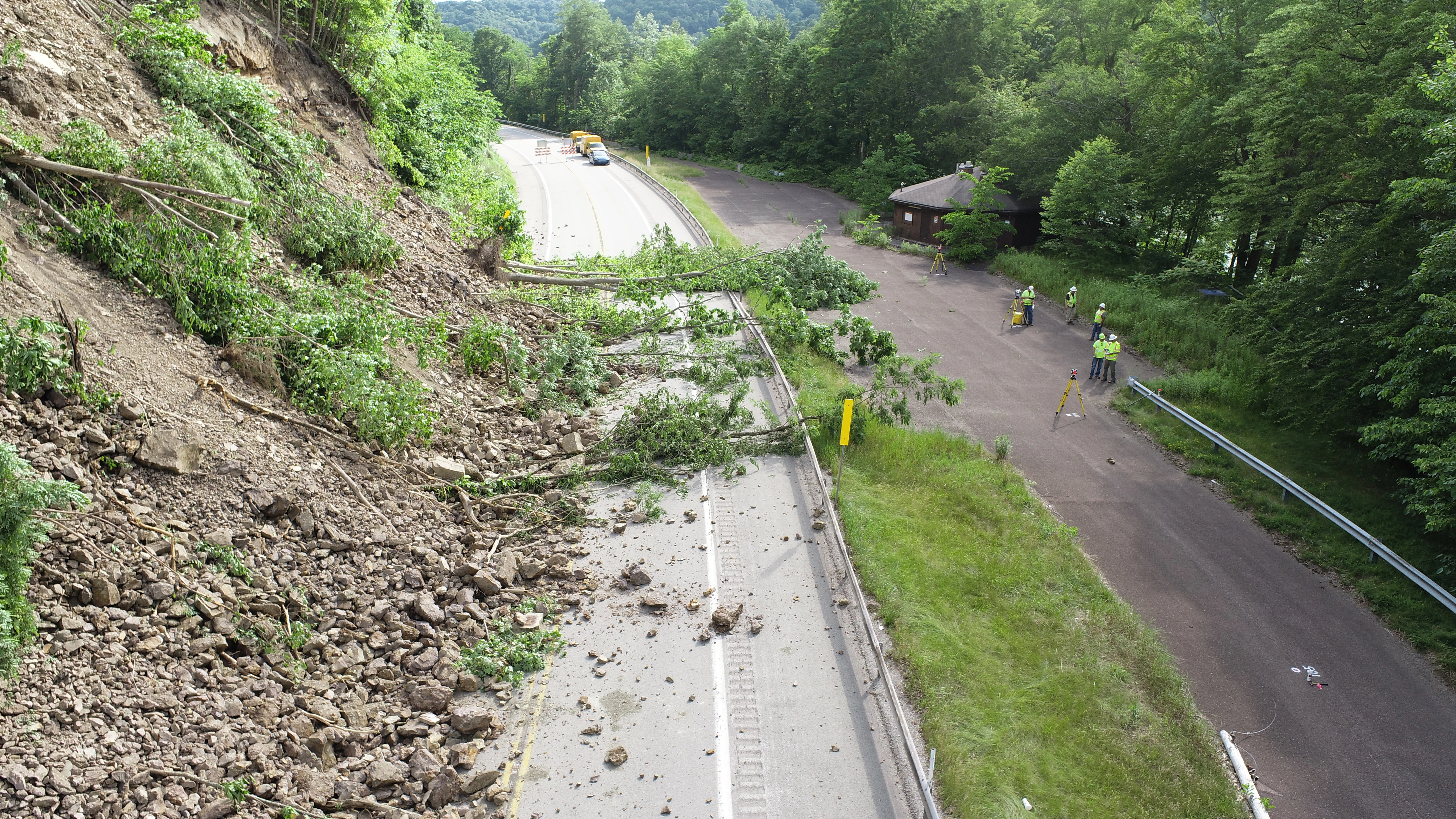 An aerial image taken from a drone shows construction workers assessing a roadway covered with fallen trees and other debris due to a landslide.