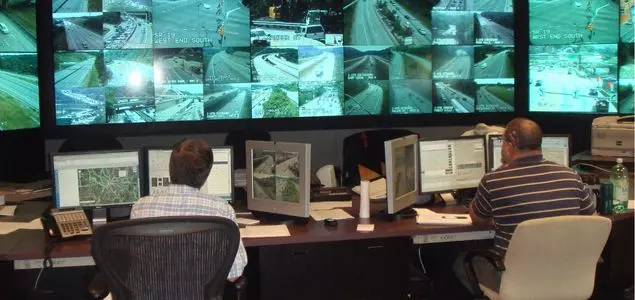 An image showing two workers in front of several computer screens and a large bank of monitors that display webcam images of roadways.