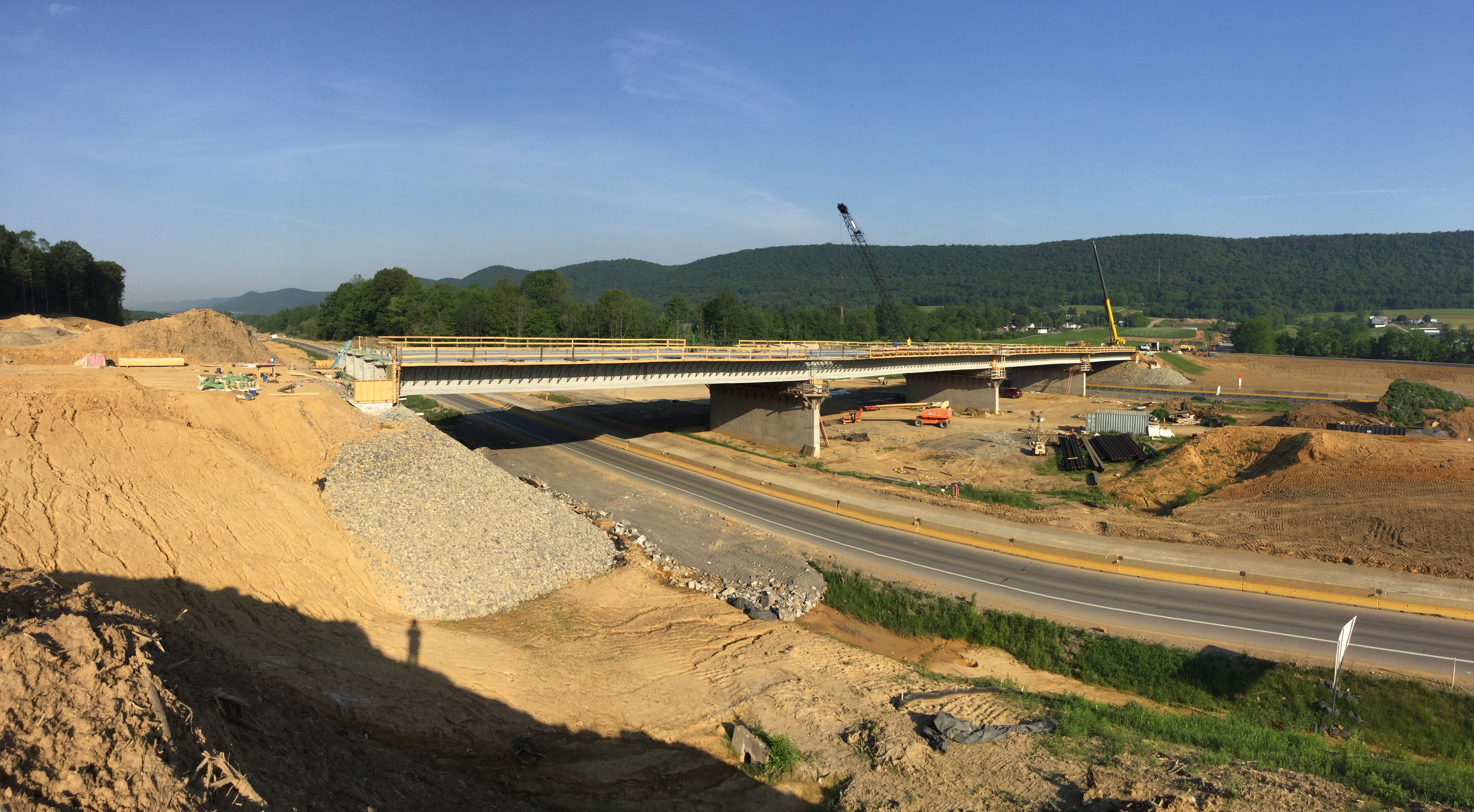 Panoramic view of a bridge crossing a roadway with tan dirt mounds on either side.