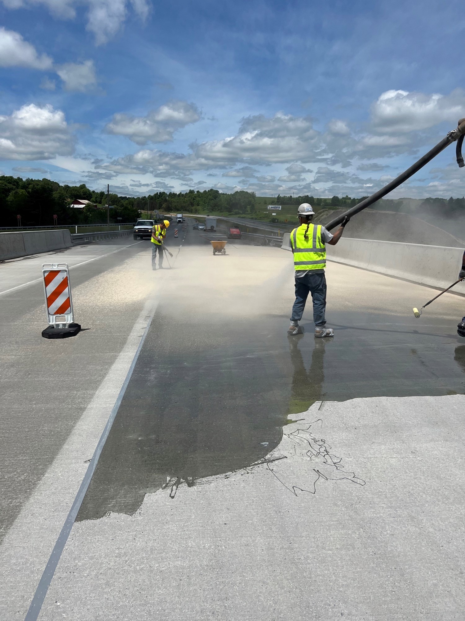 Construction crew members spray a liquid material on a bridge.