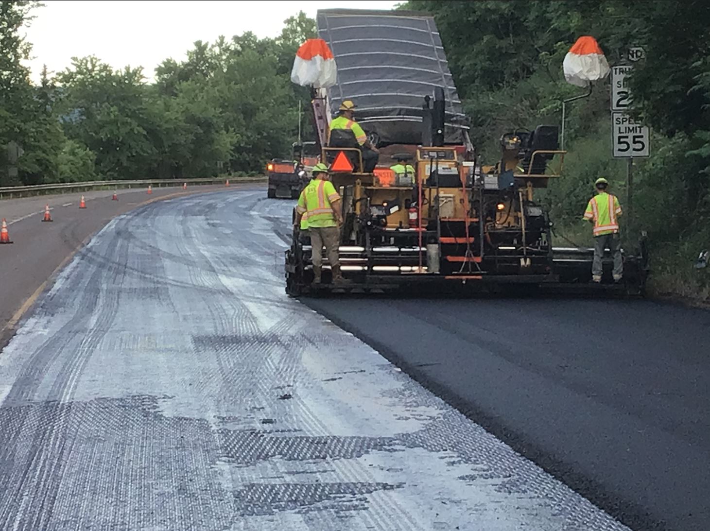 A large construction vehicle places and smoothes asphalt onto a milled roadway.