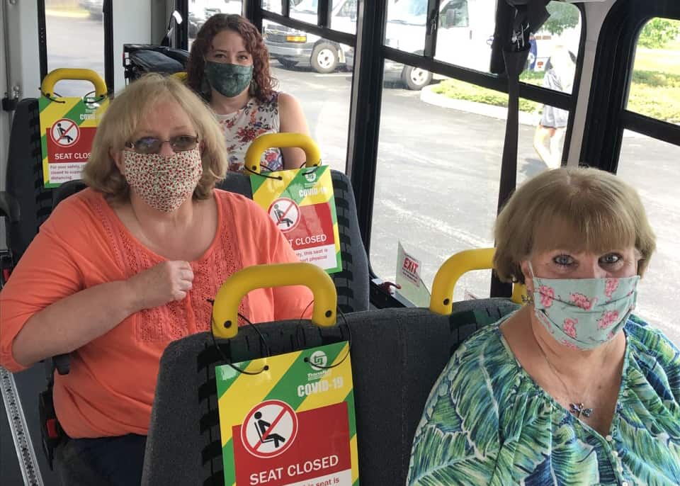 Three women wearing cloth face masks sit in a bus.
