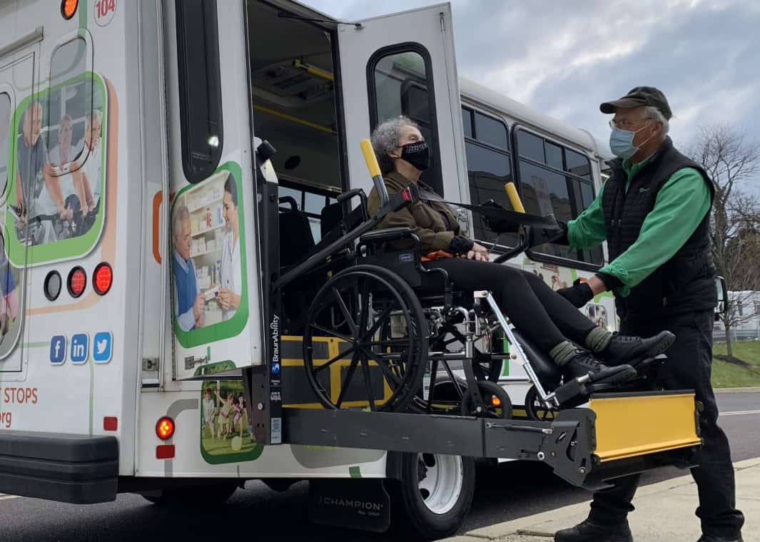 A man assists a woman in a wheelchair getting on a bus.