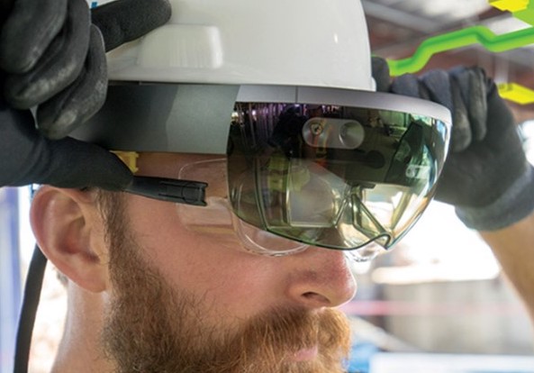 Construction worker conducting an inspection using the Microsoft HoloLens augmented reality tool that is attached to the hard hat. 