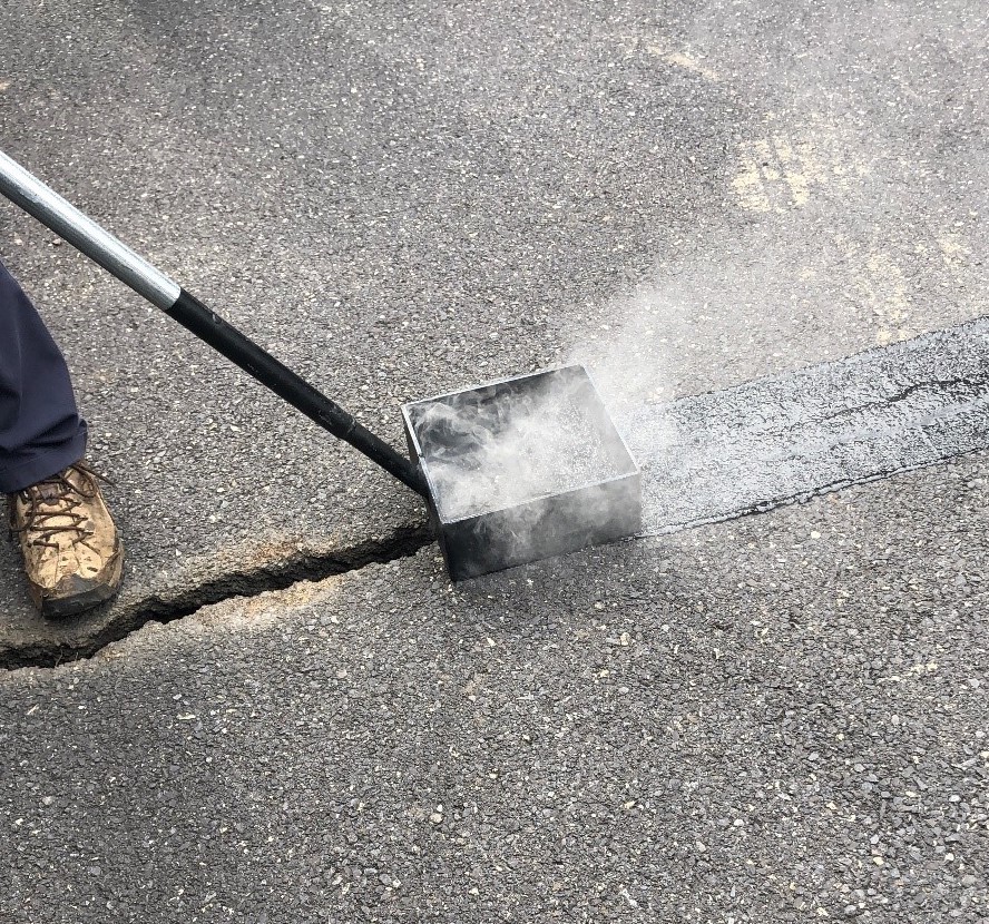 Highway maintenance worker applying hot pour mastics to a crack on a road.