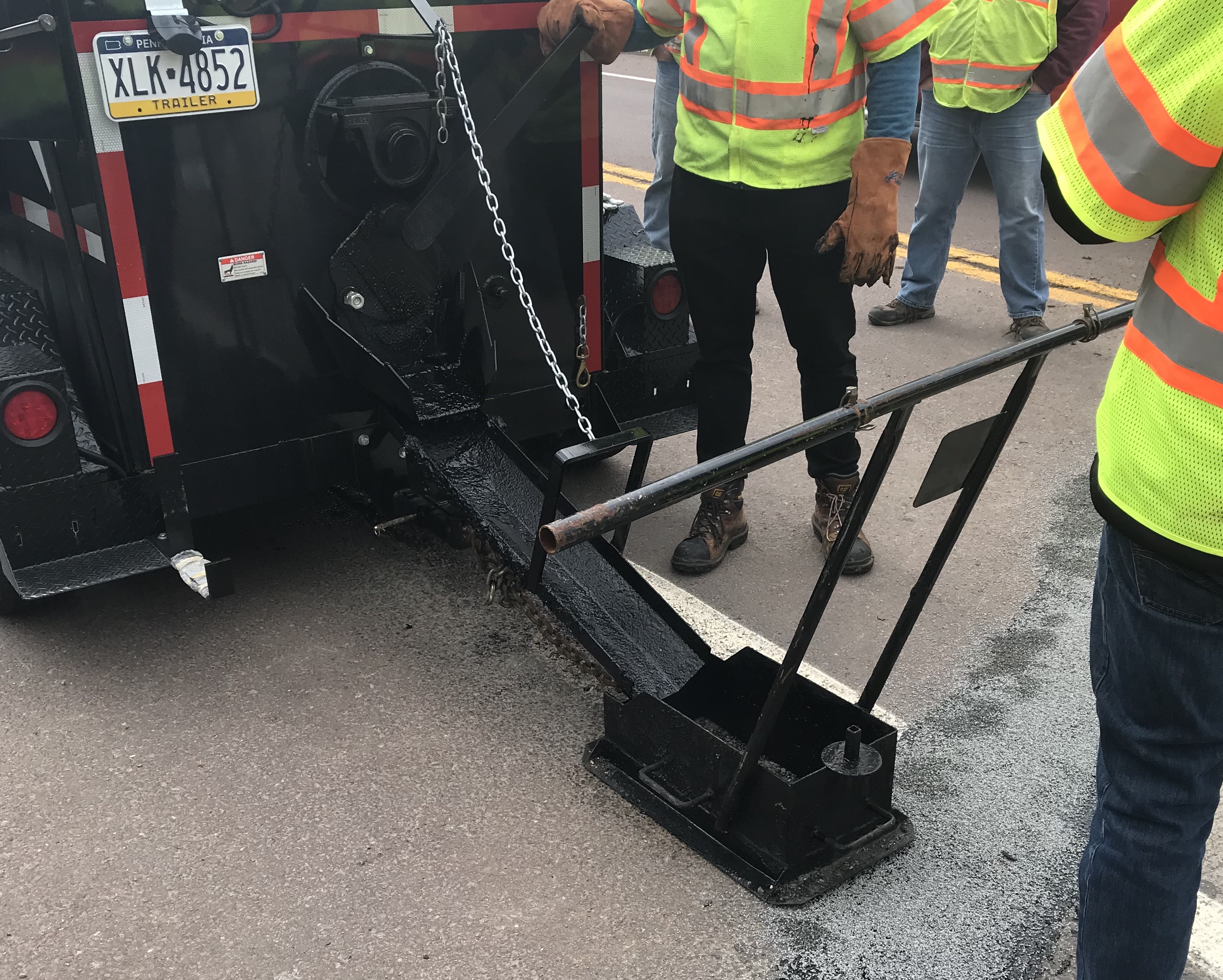 Highway maintenance workers feeding hot pour mastics into equipment before applying it to a road.