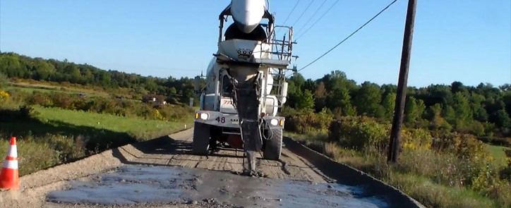 Large cement truck pouring slurry on a dirt roadway.