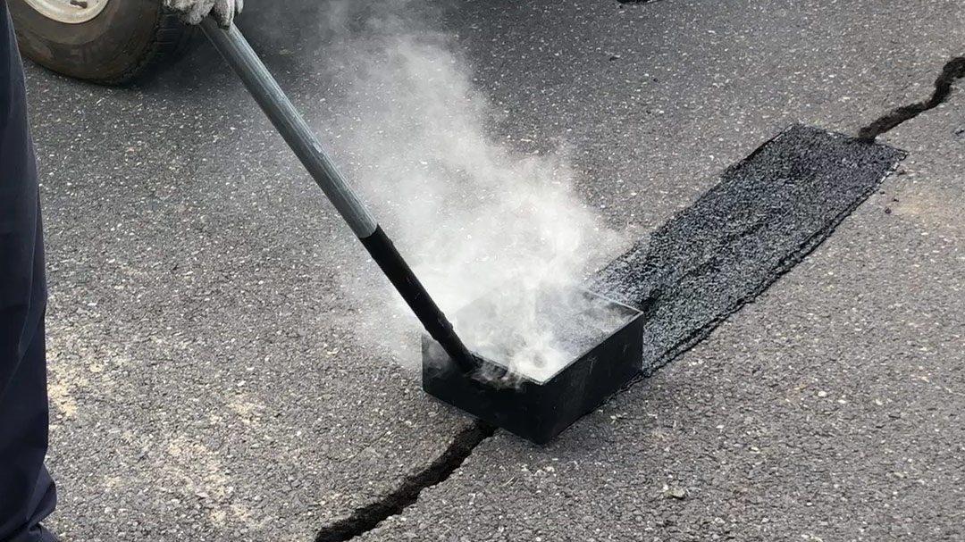Man using applying black, oil-like material that is steaming to a crack in roadway.