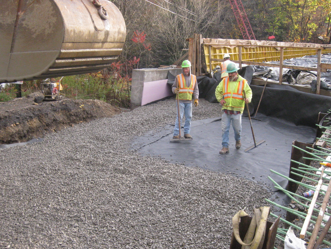 Construction workers spreading gravel over a tarp dumped by an excavator.