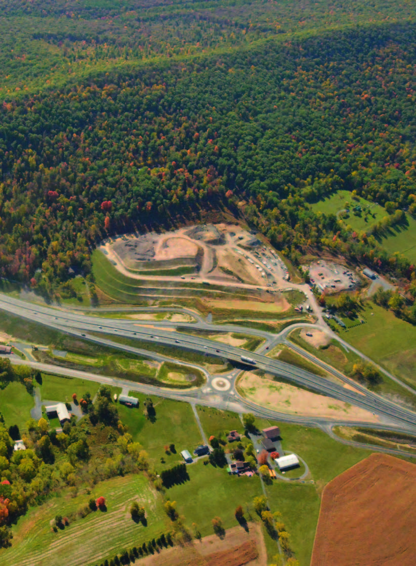 Aerial view of four-lane roundabout connected to a new highway in the midst of sprawing fields.