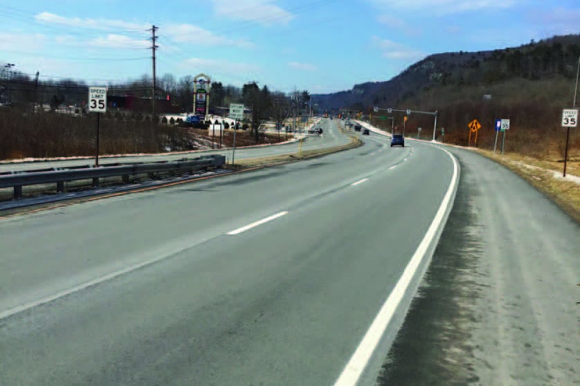A freshley paved two lane highway goes into the distance with mountains in the background.