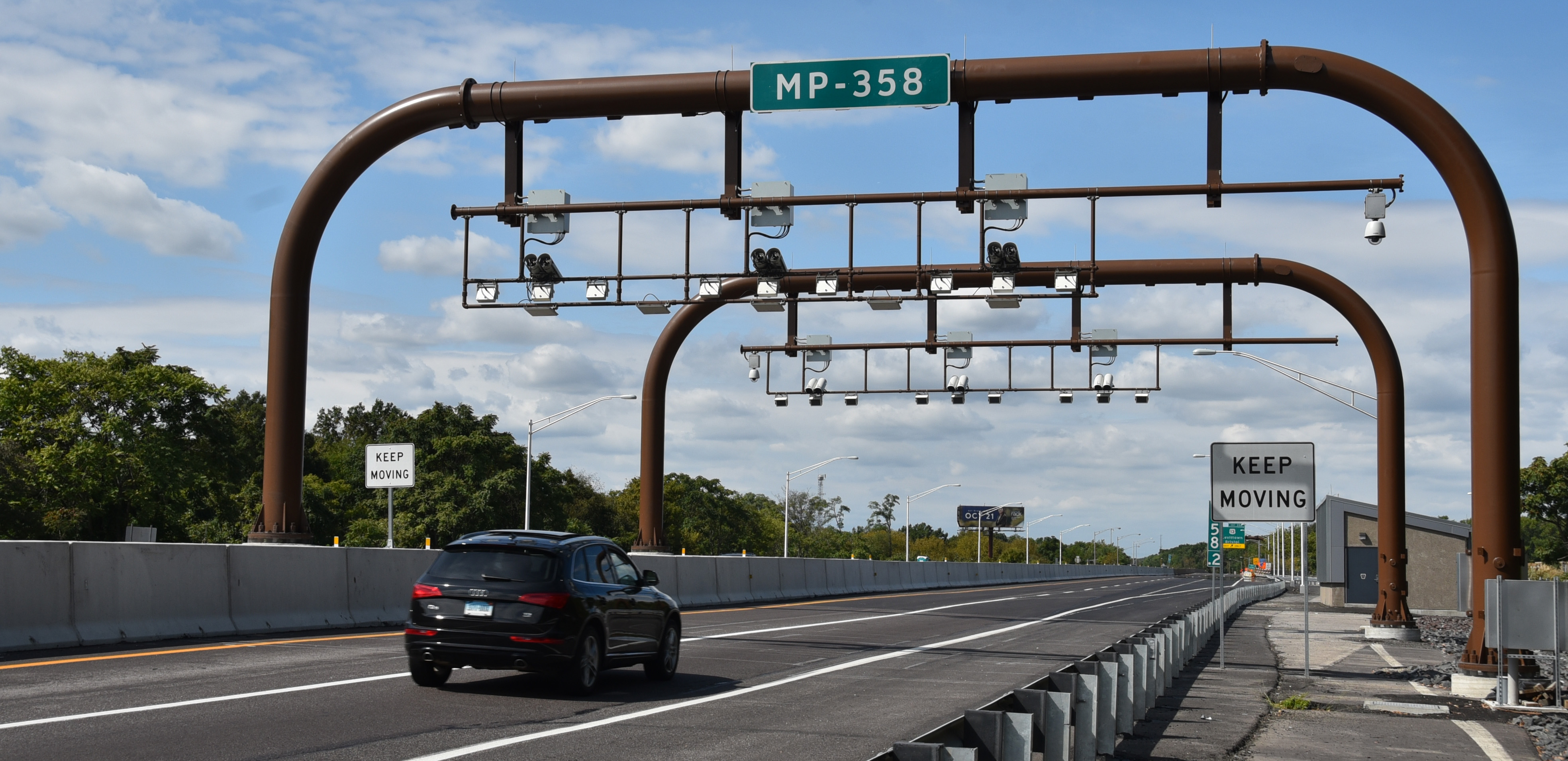 Two curved metal beams with mounted cameras over a two-lane highway.