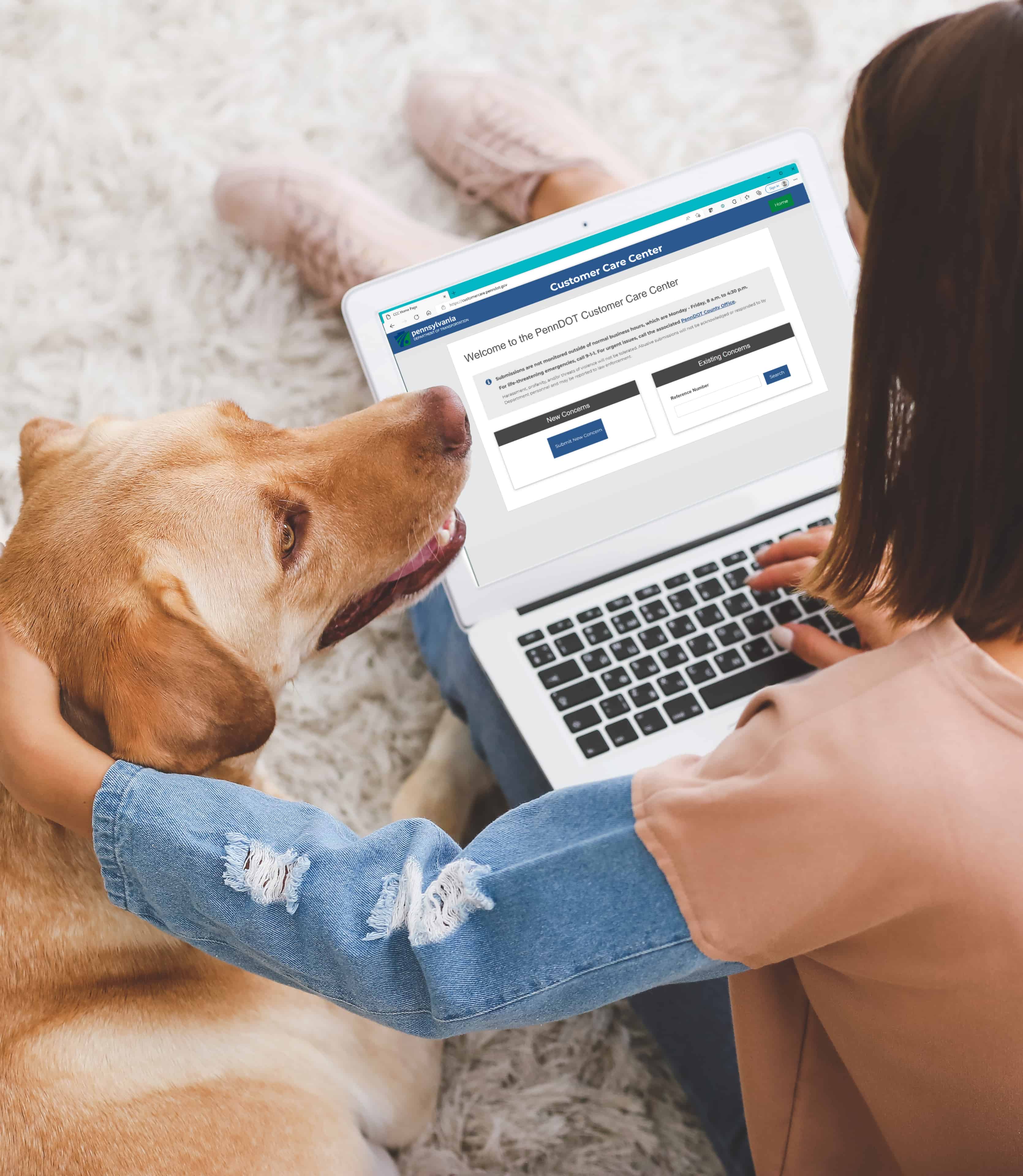A woman sitting on a white carpet with her dog. A laptop rests in front of her, open to the PennDOT Customer Care Center website.